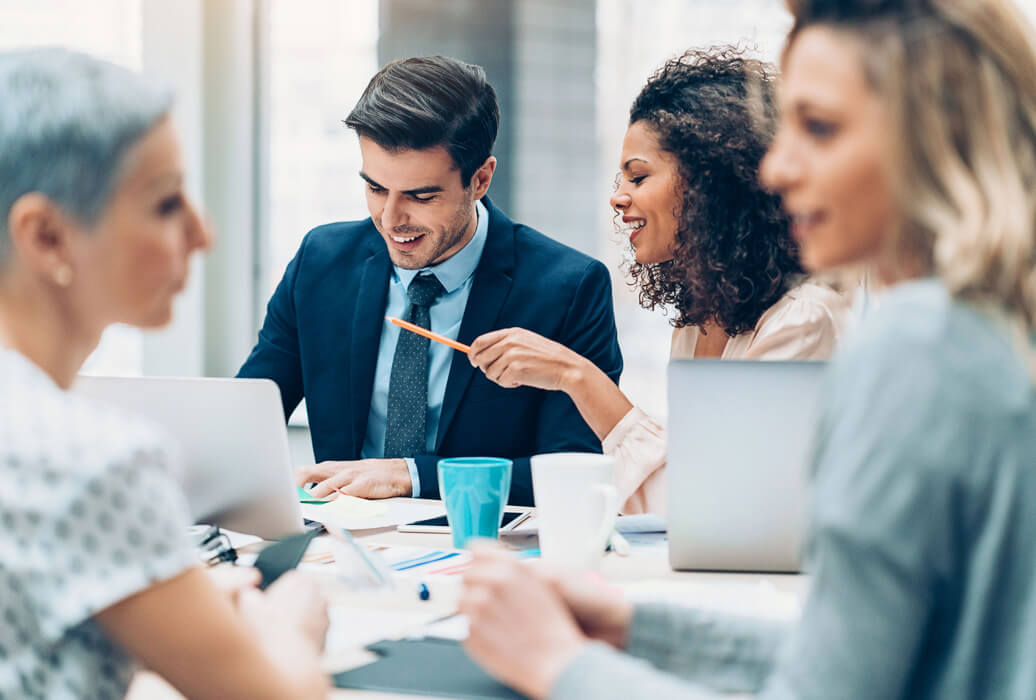 stock photo – 4 workers in office 3 women/1 man Colleagues share a laugh at break time in a small office meeting